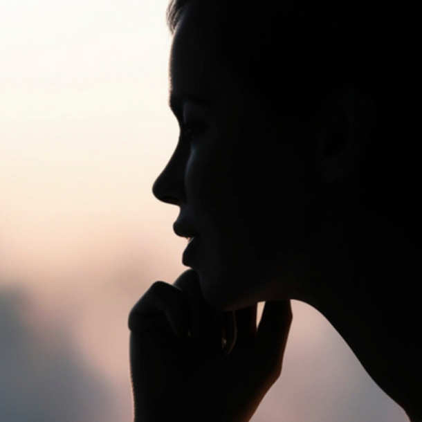 A person’s silhouette by a bright window, hand to chin, deep in thought, evoking the quiet weight of anxiety at work.