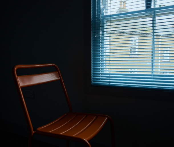 An empty office chair beside window blinds in a dim room, a visual metaphor for resenteeism and a mentally checked-out employee still at the desk.